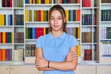 Portrait of a confident teenage schoolgirl looking at the camera in the library.