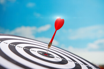 Red dart in center of dartboard over sky