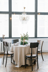 A dining table with wooden chairs, decorated and served for Christmas dinner against the background of a large window in the house, a crystal vintage chandelier hangs above the table