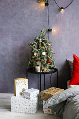 Small christmas tree on the bedside table and gifts near the bed in stylish bedroom