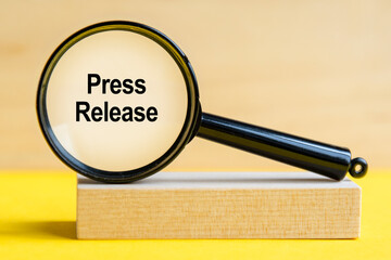 Press Release word through magnifying glass on wooden background