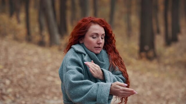 Young Red-haired Woman Freezes in Autumn Park. Female Trying To Keep Warm In Cold Outdoors.
