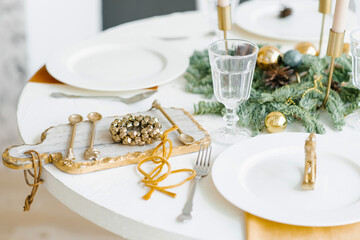 Christmas decor of the festive table for dinner. Golden wreath of bells on a beautiful cutting board and cutlery