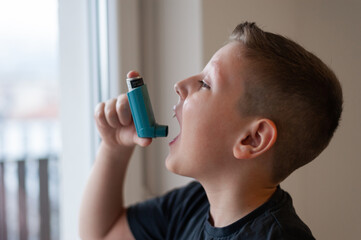 Young boy using asthma inhaler near the window, isolated at home