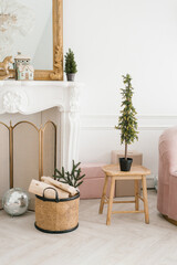 Christmas and New Year decor of the living room: firewood in a basket near the fireplace, a Christmas tree in a pot on a stool