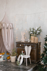 Interior of a children's room decorated for Christmas. Awning bed with toys and pillows, a tree, a wardrobe and an armchair in gray beige colors