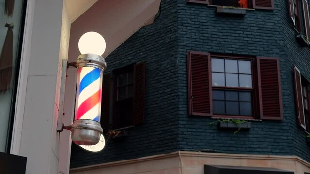 Traditional blue, red and white striped pole turning outside. Rotating lantern near barbershop. Men hairdresser symbol. International barbershop sign on wall