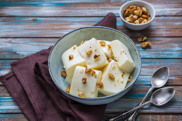 Dessert, cut into pieces of sour cream or cream jelly, garnished with walnuts  in a gray ceramic bowl on a wooden background. Jelly recipes.