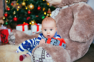 Cute little boy with gift box in hands laying on fury teddy bear. Child in white blue shirt in new year decoration