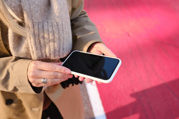Woman is holding a modern smartphone, sending a text message or using an app on her mobile phone. Internet technology user. Smartphone close-up. Focus on the phone screen