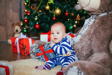 Cute little boy with gift box in hands laying on fury teddy bear. Child in white blue shirt in new year decoration
