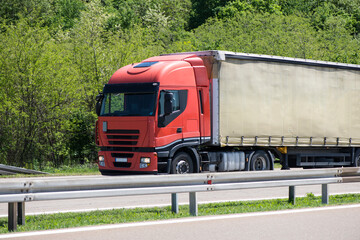 Red truck driving on asphalt road in a rural landscape.