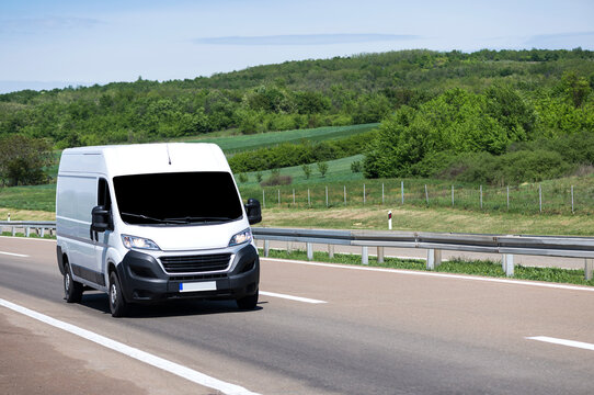 White modern delivery small shipment cargo courier van moving fast on motorway road to city urban suburb.