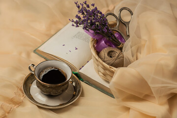 The atmosphere of a romantic morning, coffee in bed. A cup of coffee, an open book and a bouquet of lavender on a silk bed in French style. Home interior. Lifestyle. 