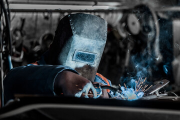 Welder industrial worker in the protective shield is engaged in welding and metal work at the plant