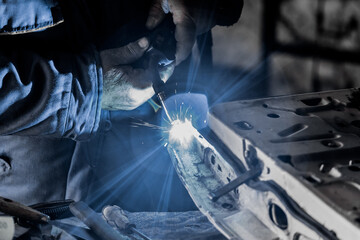 The hands of a male welder are engaged in welding and metal work close-up in the working shop of an industrial plant