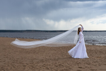 Happy young girl in a white dress on the river bank. Stormy sky in the clouds