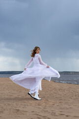 Fototapeta na wymiar Happy young girl in a white dress on the sandy shore. Thunder Sky