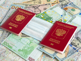 Two Russian passports are on dollar and euro bills. A medical mask is attached between the passports. The concept of traveling during a pandemic and diseases