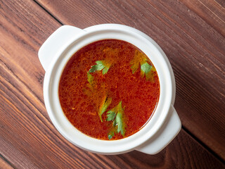 Close-up of soup borscht in a white ceramic soup bowl on a wooden background. Traditional soup for Russia and Ukraine. Greens float on top of the soup. Top view, flat lay