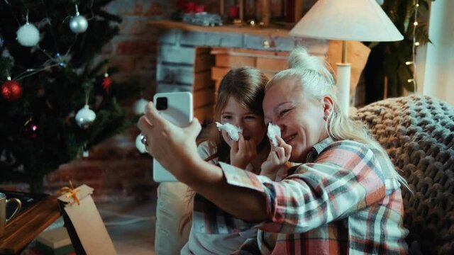 Grandmother and little girl at home funny faces for selfie on mobile phone during the winter holidays