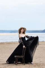 Happy young girl in a straw hat and in a black dress on the bank of the river. Thunder Sky