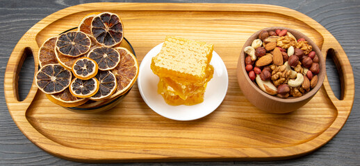 assortment of nuts and assorted dried citrus fruits and fresh floral honeycomb honey on kitchen wooden board. useful vitamin food for the human body