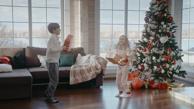 Boy and girl are happily jumping with gifts on Christmas morning. Christmas morning in big and bright house. Kids are excited to get their presents. 50 fps