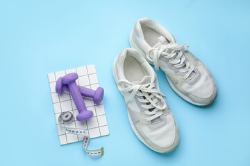 Dumbbells, shoes and measuring tape on blue background
