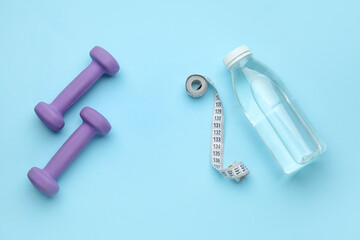 Dumbbells, measuring tape and bottle of water on blue background