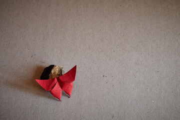 Origami red butterfly posing on a little rock on a grey grainy texture background. World origami...