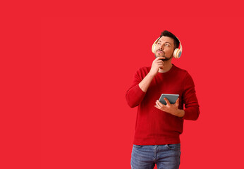 Thoughtful man with tablet computer and headphones on color background