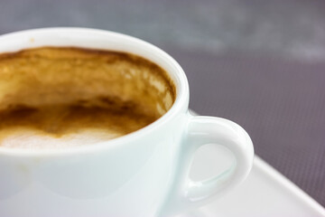 Round white ceramic cup with cappuccino latte coffee brown foam on square saucer on a table. A hot flavored aromatic drink in a cafe, restaurant in the morning, lunch time. Beverage theme, copy space.