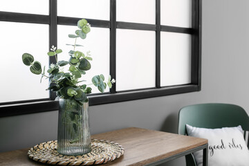 Glass vase with eucalyptus on shelf near window in dark room