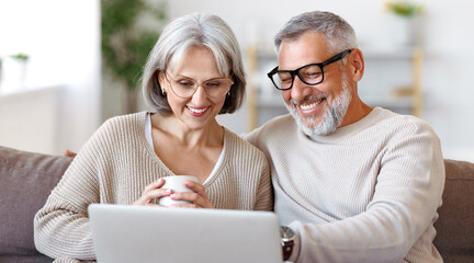 Happy senior family couple watching comedy or funny video on laptop while spending free time at home