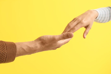 Fototapeta premium Man holding woman's hand on yellow background