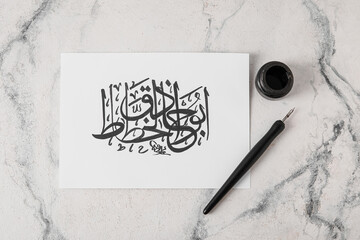 Paper with Arabic text and tools for calligraphy on light background