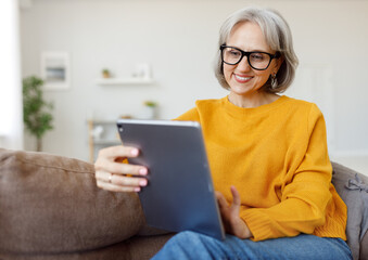 Portrait of happy smiling senior woman resting relaxing on sofa with tablet at home