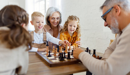 Children brother and sister playing chess while sitting in living room with senior grandparents