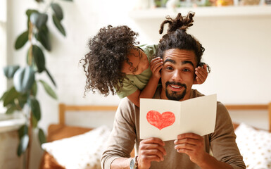 Smiling afro american boy son covering eyes of father with hands and congratulating him on holiday