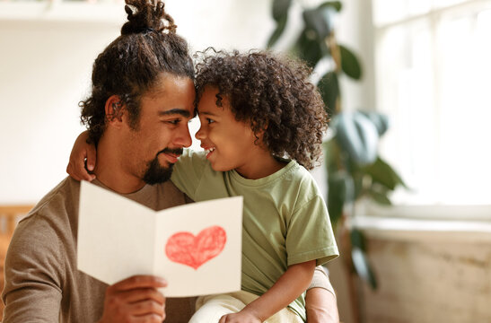 Cute african american little boy son giving his father handmade greeting postcard on Fathers Day