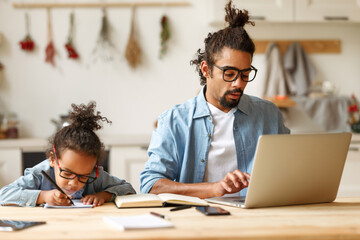 Young african american dad working remotely on laptop with child son at home