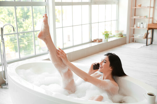 Relaxed young woman talking by mobile phone while taking bath at home