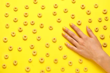 Gordijnen Woman with beautiful manicure and cereal rings on yellow background © Pixel-Shot