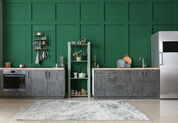 Interior of modern kitchen with shelving unit and green wall