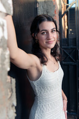 Fototapeta premium Confident high school senior girl spans her arms in rustic brick building doorway posing in her lace white dress