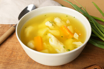 Bowl of tasty dumpling soup on wooden board, closeup