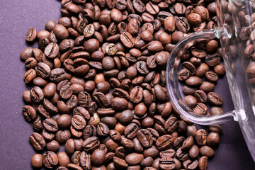 Fototapeta premium Coffee beans isolated on purple background. Transparent coffee cup laying on top of coffee beans.