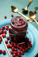 Jar of tasty cranberry jam and fresh berries on green background