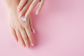 A young woman is applying cream to her hands. Spa and body care concept on a pink background. Image for advertising.